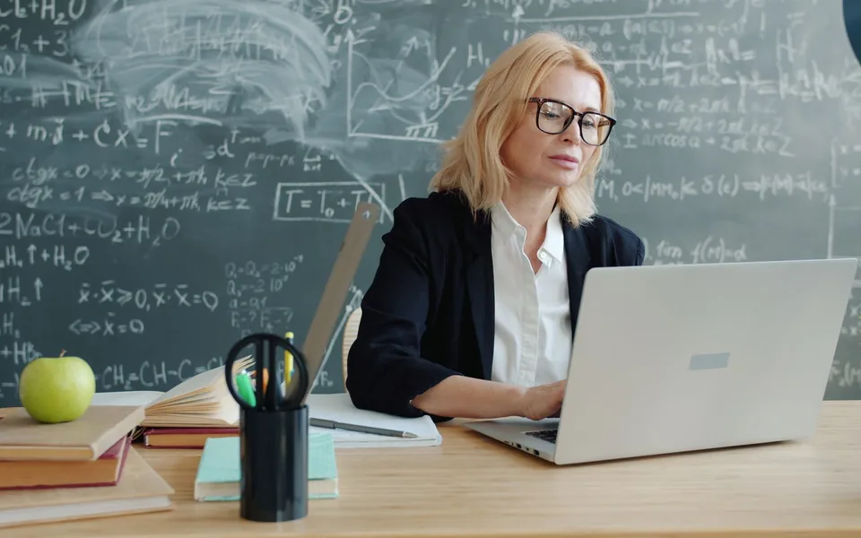 Profesora preparando la clase con su portátil delante de la pizarra